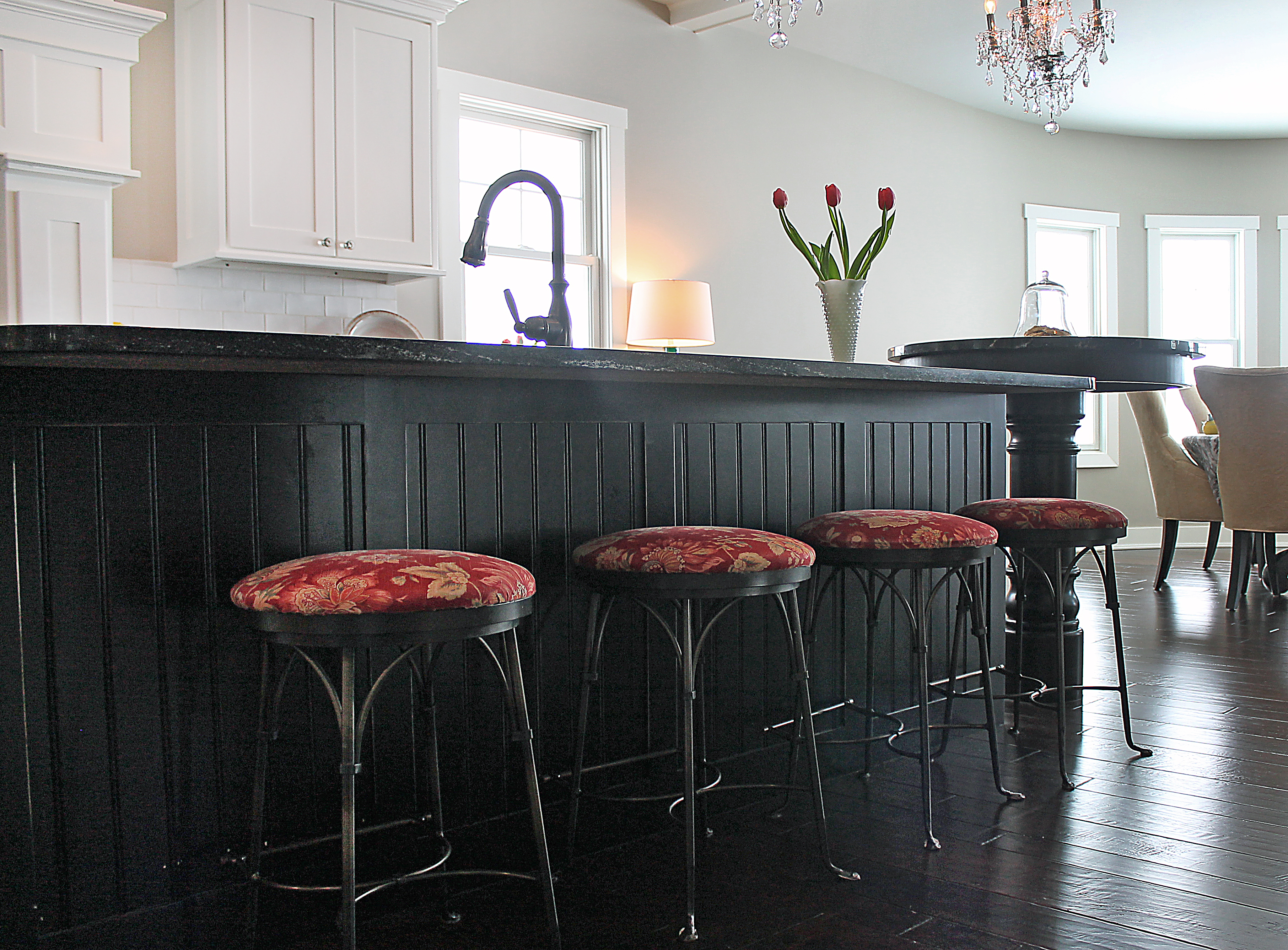 Elegant black beadboard island with red floral bar stools and crystal chandelier